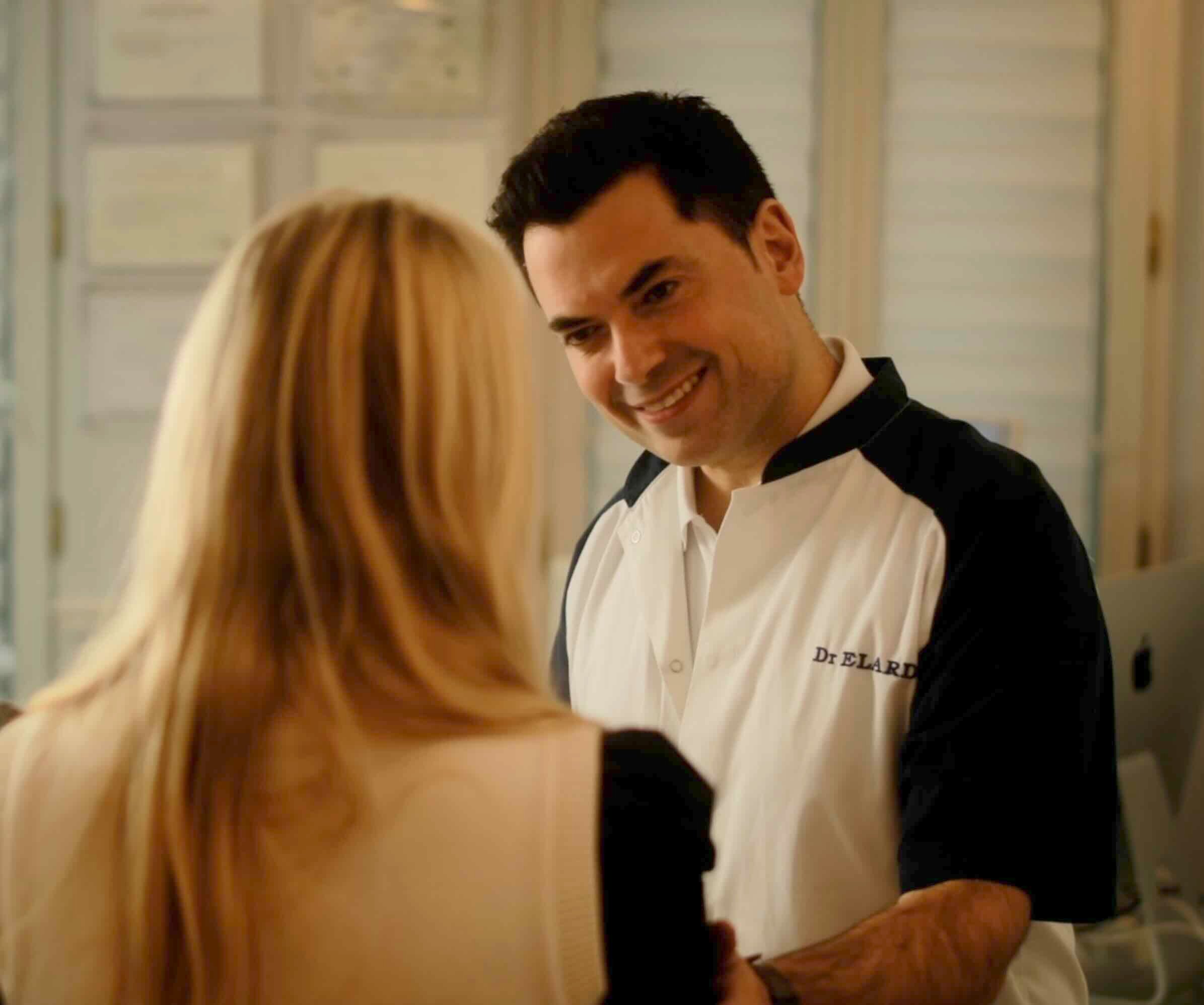 Dr. Elard warmly greeting a patient during a consultation, reflecting professionalism and trust in an aesthetic clinic setting